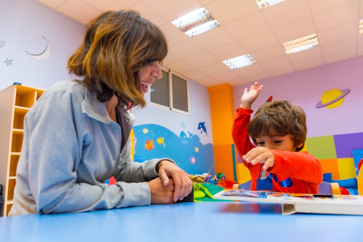 portrait-female-teacher-with-child-sitting-reading-story-book-indoor-kindergarten